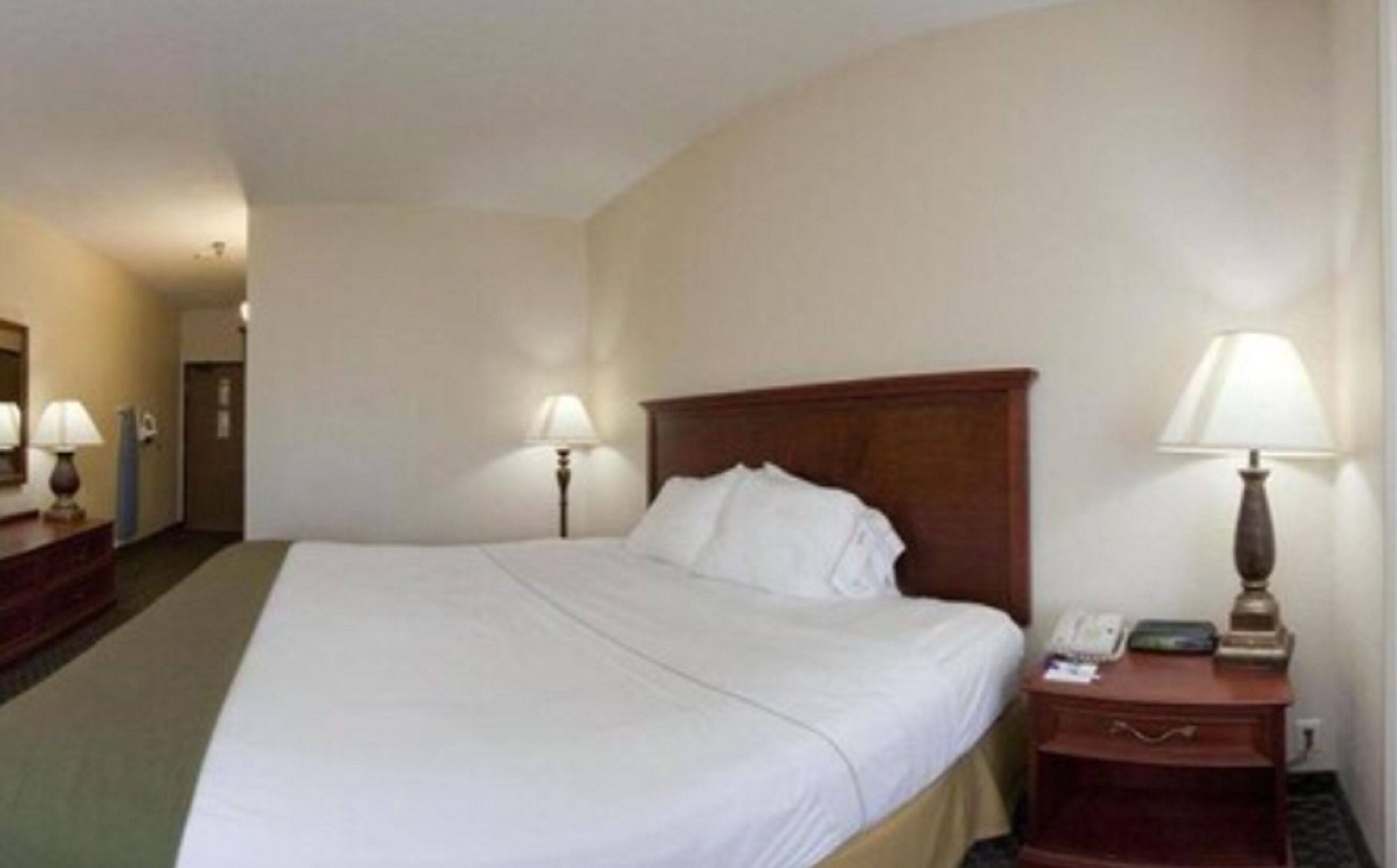 A hotel room with a large bed, two bedside lamps, a nightstand with a phone, and a door in the background.