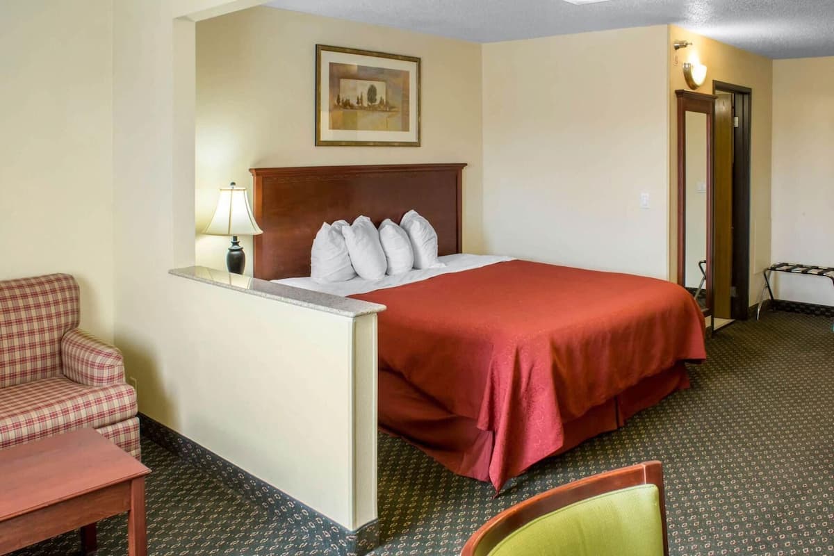 A hotel room with a bed, a chair, a desk, and a lamp.