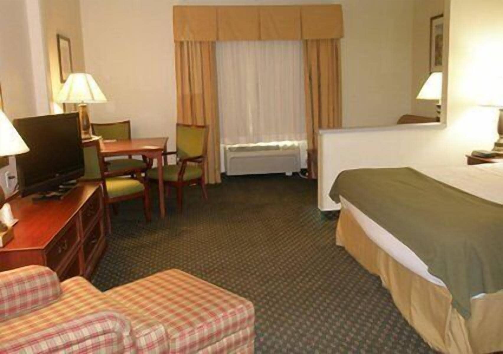 A hotel room with a bed, a desk with a television, a chair, and a small couch.