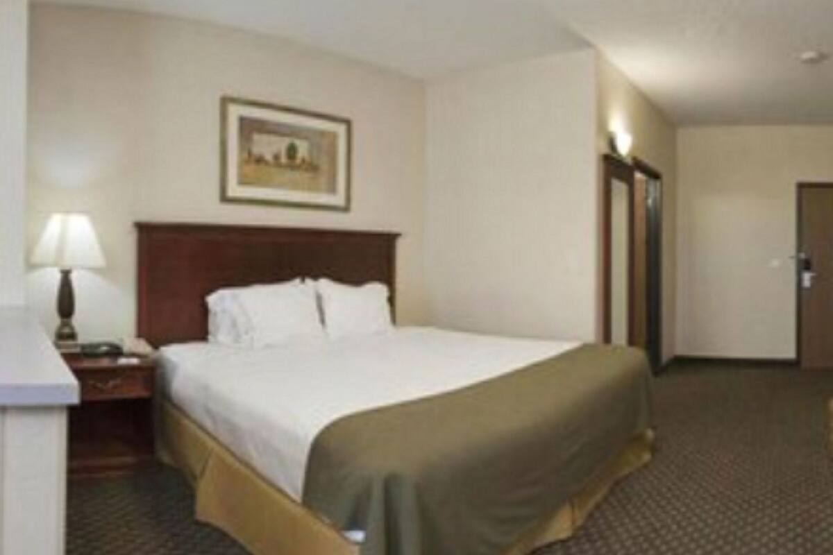 A hotel room with a bed, a nightstand, a lamp, a framed picture on the wall, and a door.