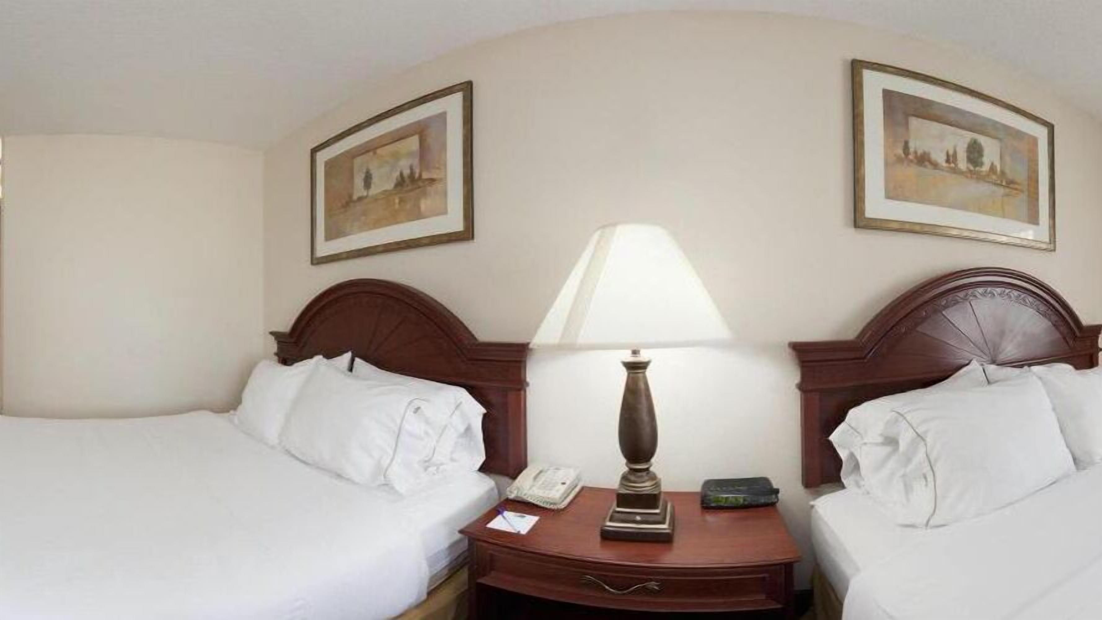 Une chambre d’hôtel avec deux lits simples, une table de chevet avec une lampe, un téléphone et deux tableaux encadrés au mur.