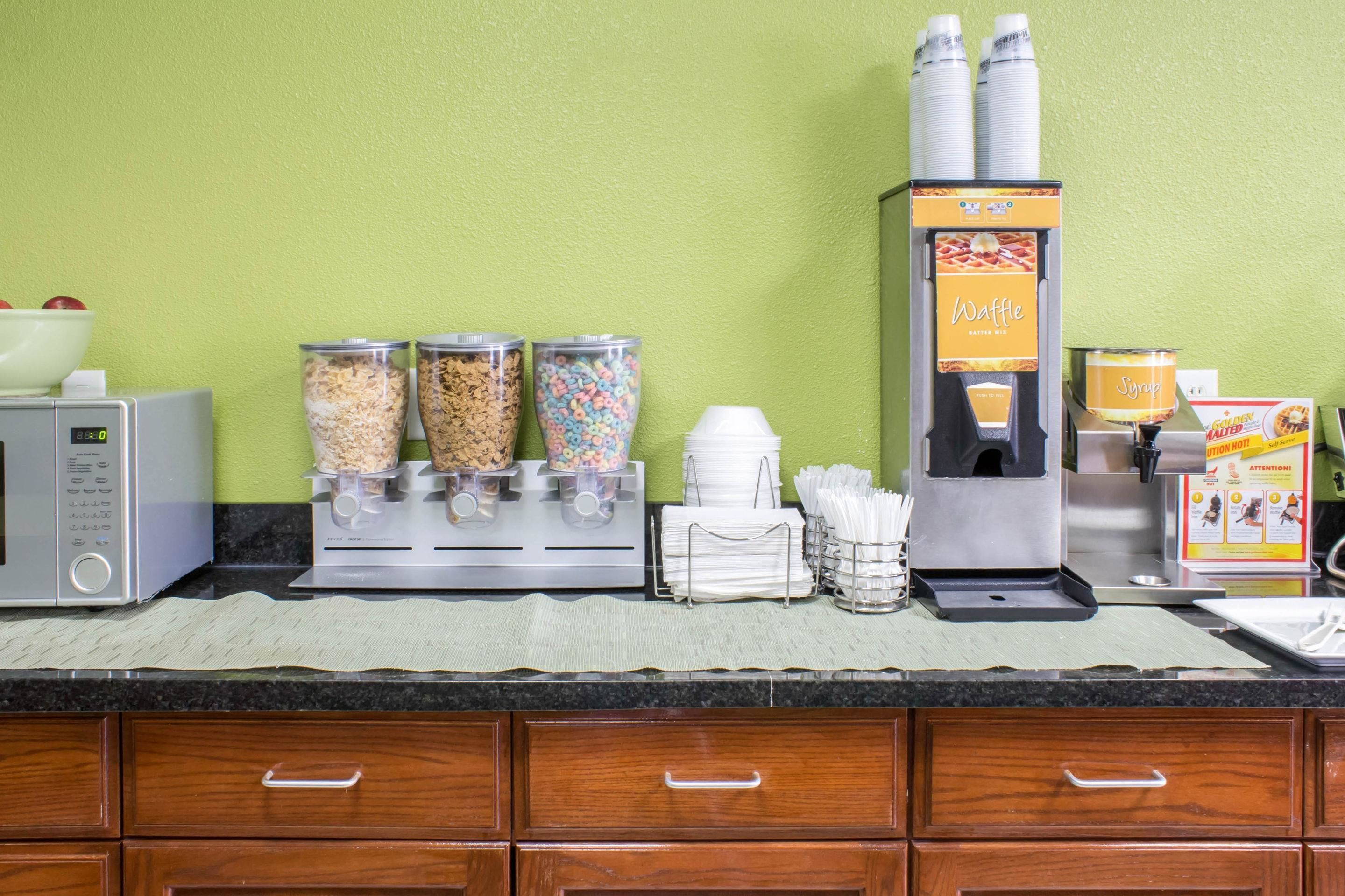 A self-service breakfast station with cereal, waffles, and syrup dispensers.