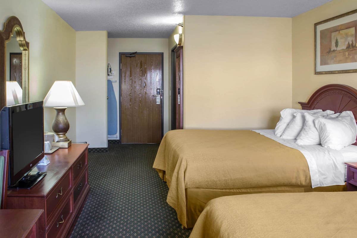 A hotel room with two beds, a TV, a lamp, a dresser, and a door leading to another room.