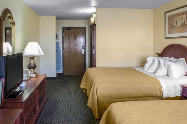 A hotel room with two beds, a TV, a lamp, a dresser, and a door leading to another room. - Quality Inn & Suites Sioux City Southeast (Sioux City)