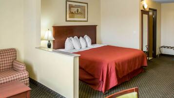 A hotel room with a bed, a chair, a desk, and a lamp.