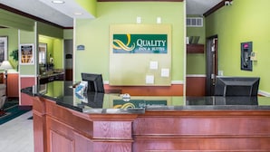 Una mesa de recepción con un cartel de Quality Inn & Suites, un letrero de no fumar y una cámara de seguridad.