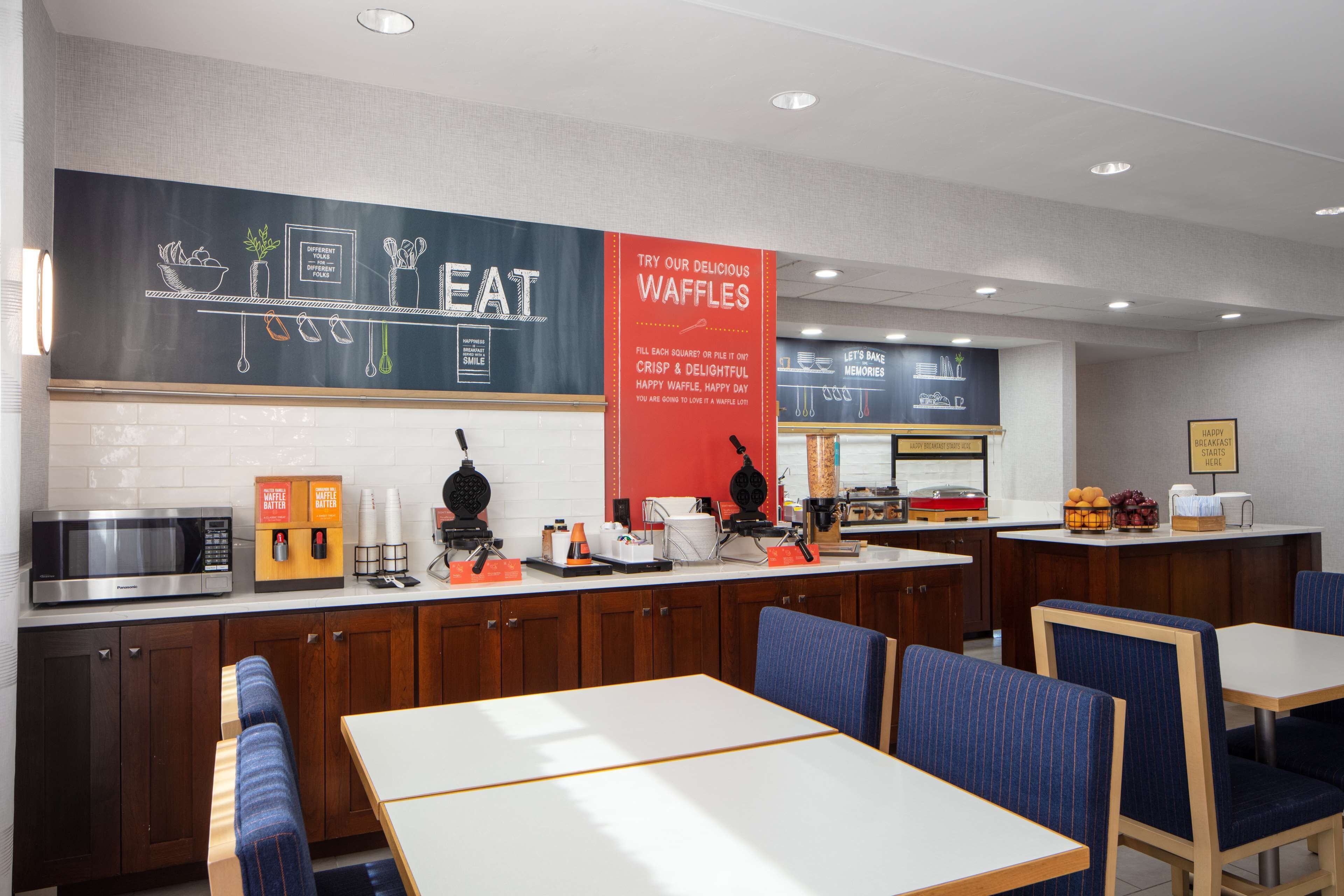Una cafetería moderna con un menú en pizarra, estación de gofres y zona de estar.