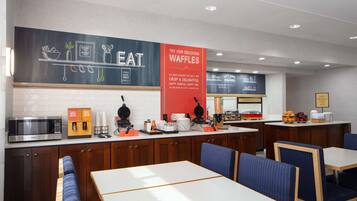 Una cafetería moderna con un menú en pizarra, estación de gofres y zona de estar.