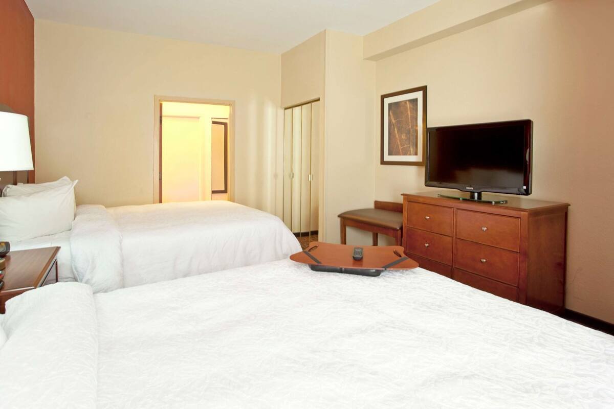 A hotel room with two beds, a TV, a desk with a lamp, a chair, and a dresser.