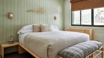 A bedroom with a bed, bedside tables, a bench, and a window with a view of buildings.