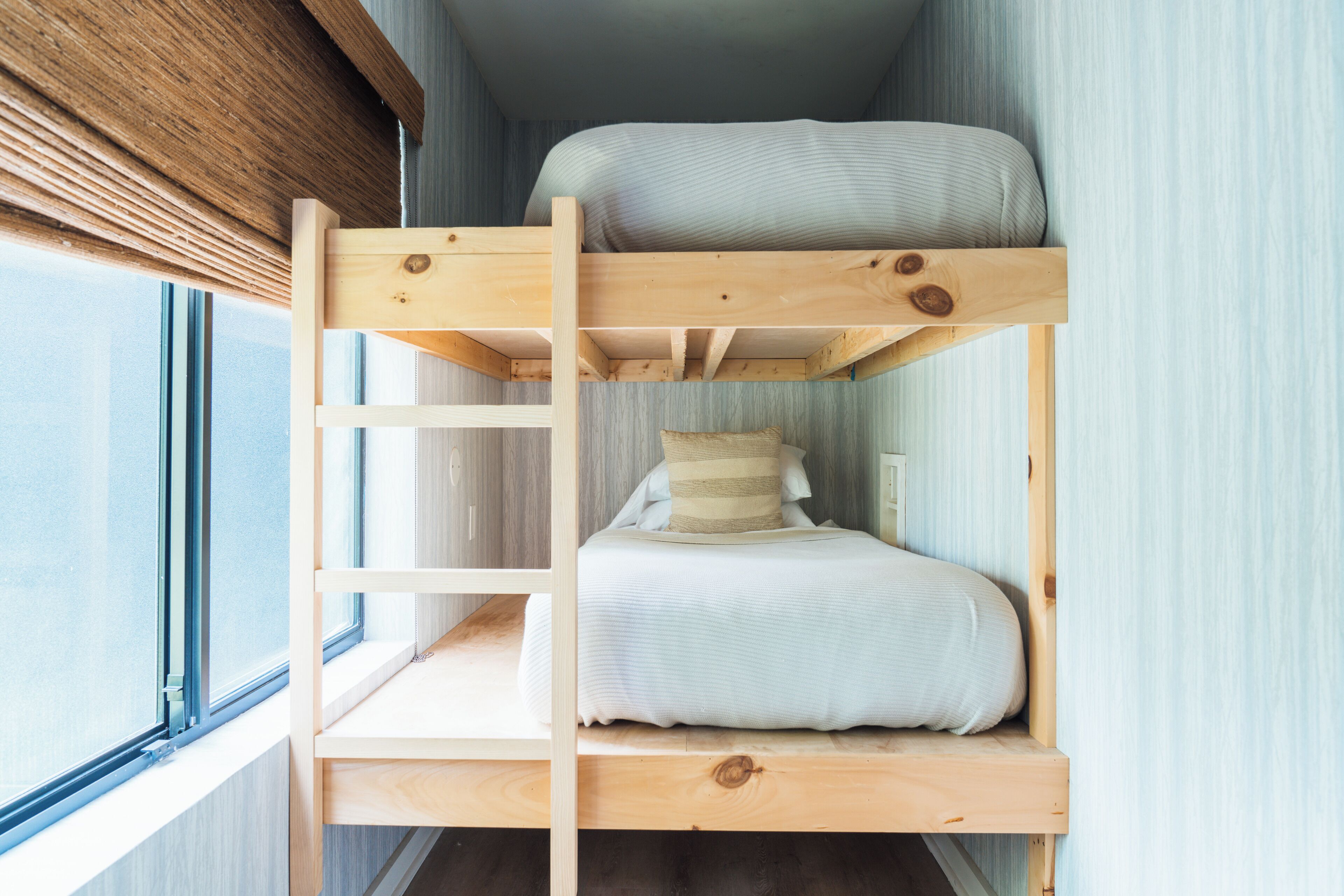 Una cama litera con escalera, una ventana y una mesita de noche.