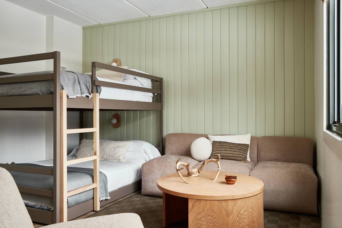 A bunk bed with a ladder, a sofa, and a round wooden table with antlers and a bowl.