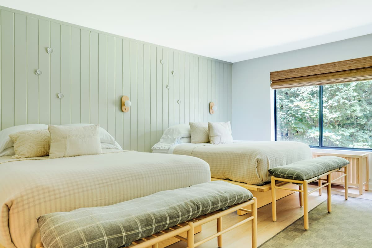 A bedroom with two beds, a bench, and a window with a view of trees.