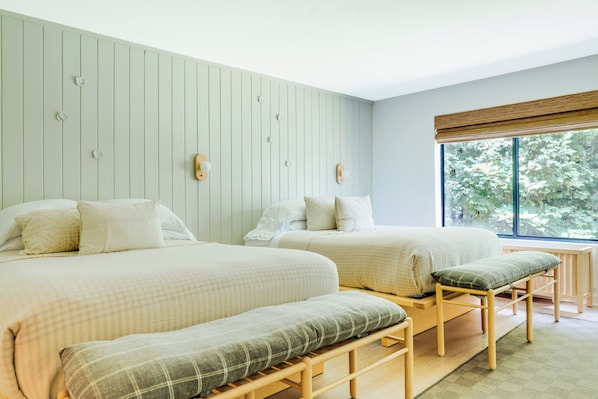 A bedroom with two beds, a bench, and a window with a view of trees.