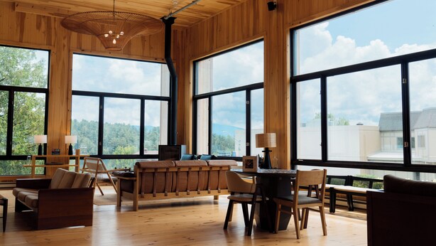A spacious room with large windows, wooden walls, and a central seating area with a table and chairs. - Laurel Lake Placid (Lake Placid)