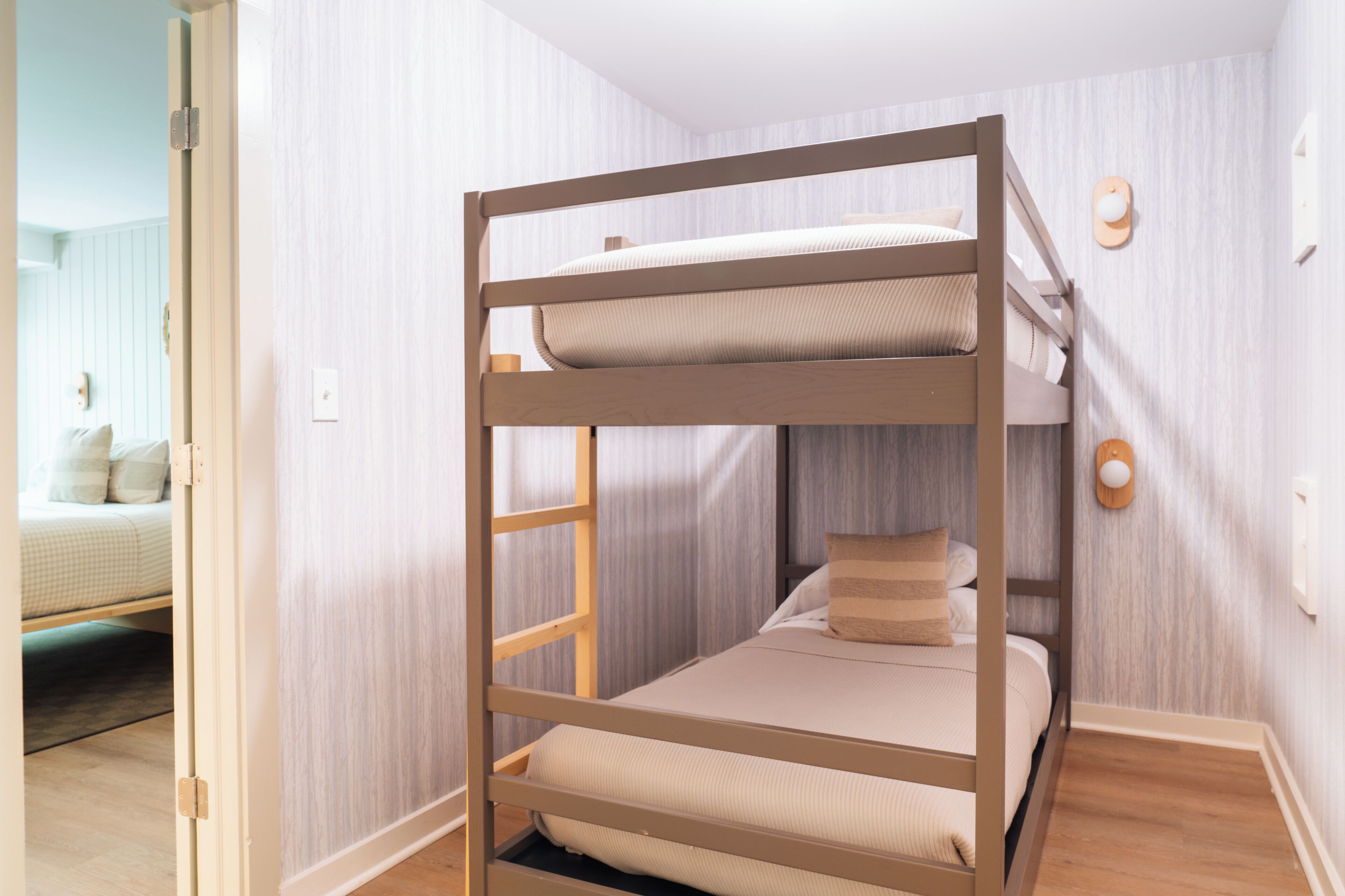 A bunk bed with a ladder, a bedside table, and a wall-mounted light fixture.