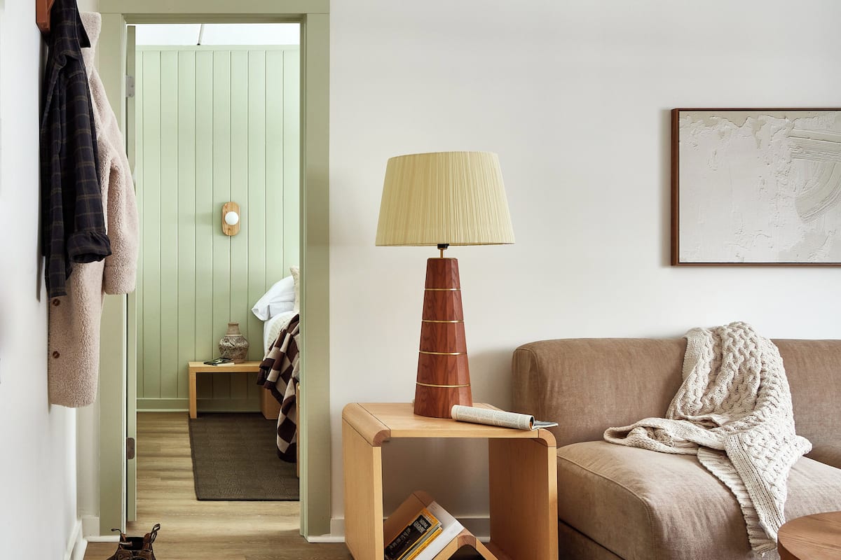 A cozy living room with a wooden side table, a lamp, a sofa, and a door leading to another room.