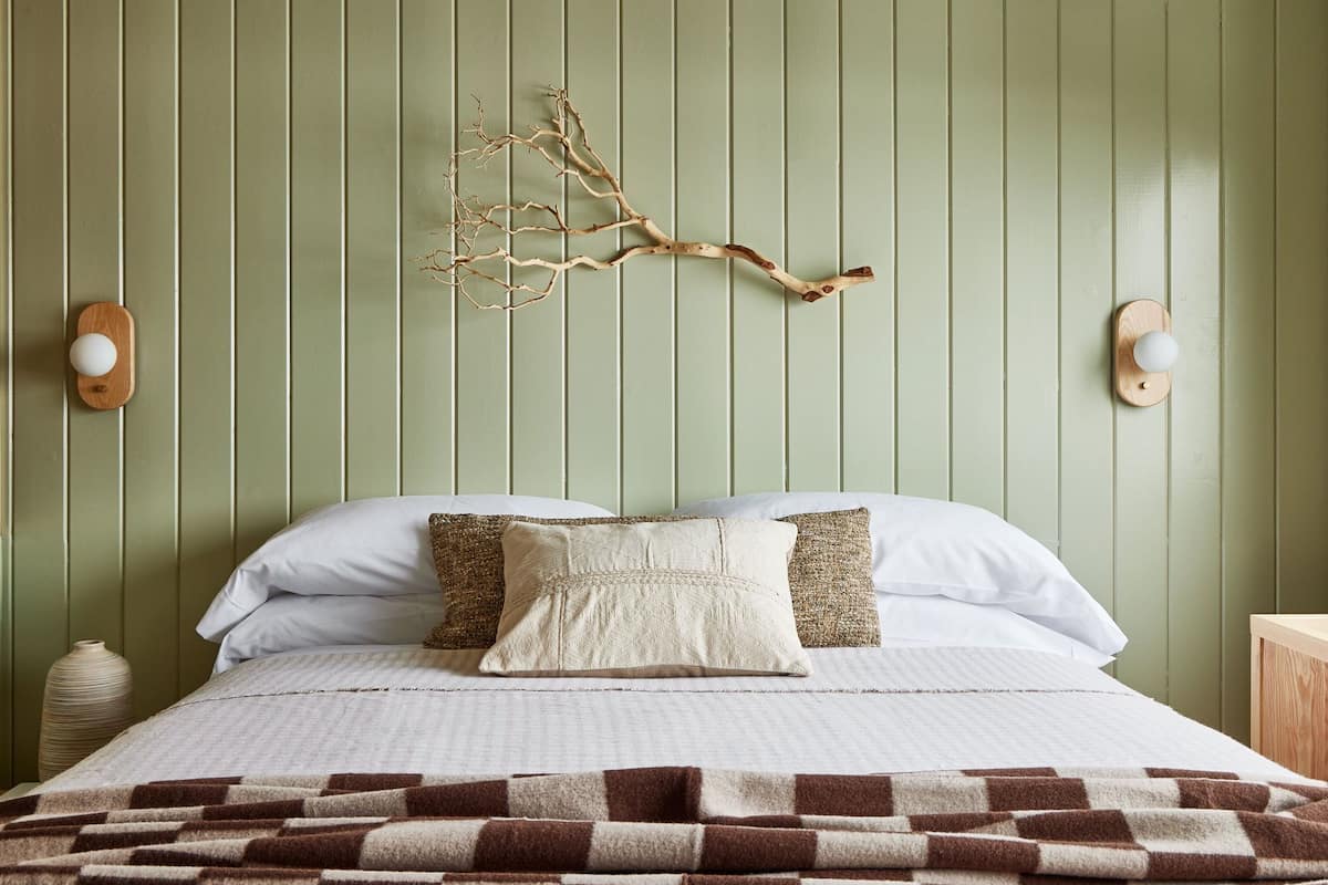 A bed with white and patterned pillows, a brown and white checkered blanket, and a wall-mounted branch decoration.