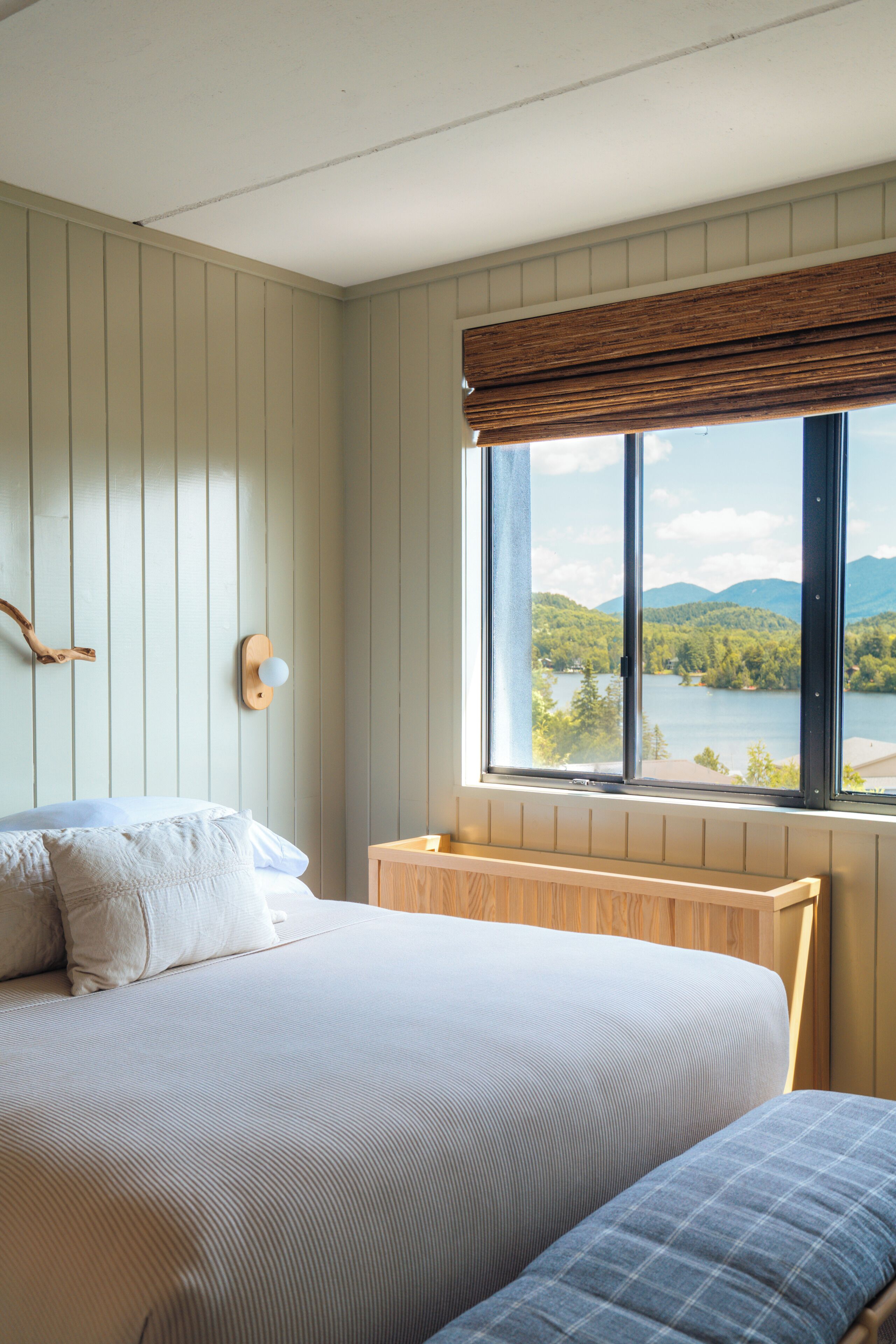 Un dormitorio con cama, ventana y vistas a un lago y montañas, además de un cabecero de madera.