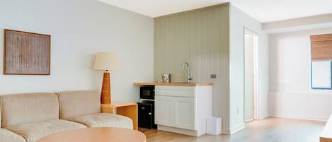 A modern living room with a sofa, a round coffee table, a lamp, and a kitchen area with a microwave and cabinets.