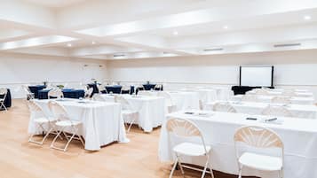 A conference room with multiple tables and chairs, a projector screen, and a wooden floor.