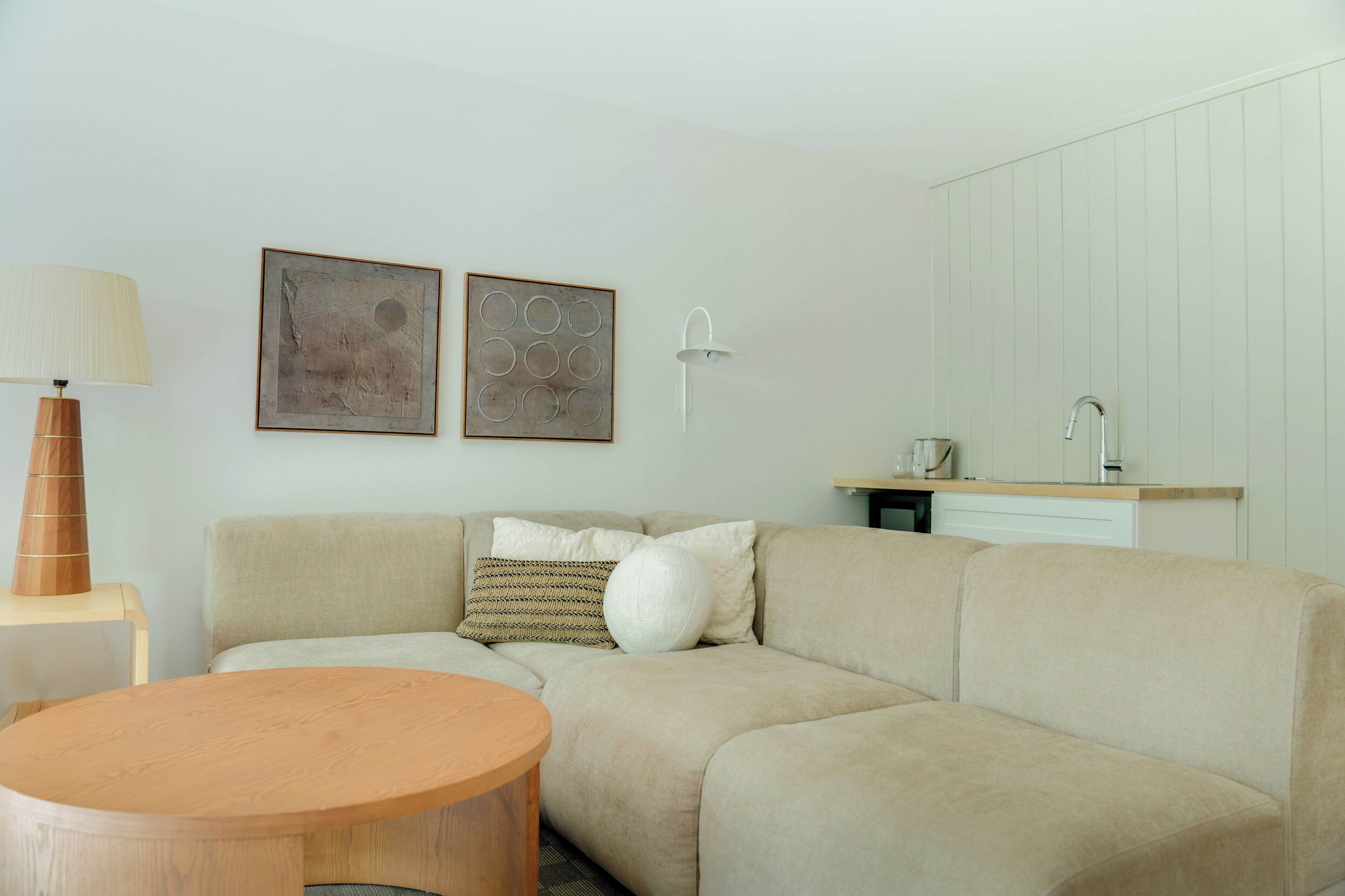 A living room with a sofa, a round wooden table, a lamp, and two wall-mounted artworks.