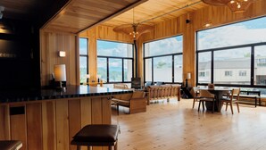 A spacious room with wooden flooring, large windows, a bar area, and seating arrangements. - Laurel Lake Placid (Lake Placid)