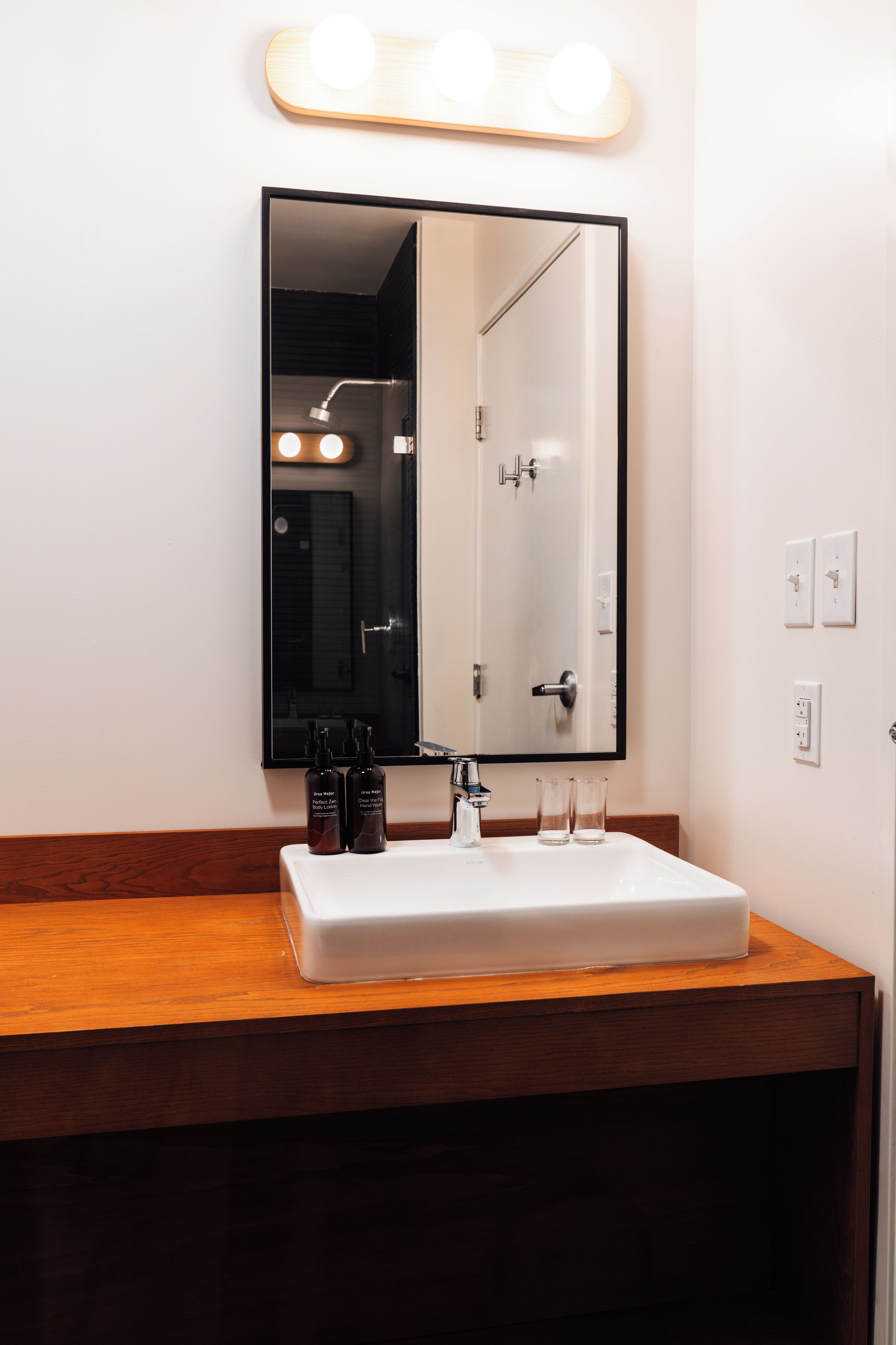 A bathroom with a white sink, a mirror with lights above it, and two bottles of lotion on the counter.
