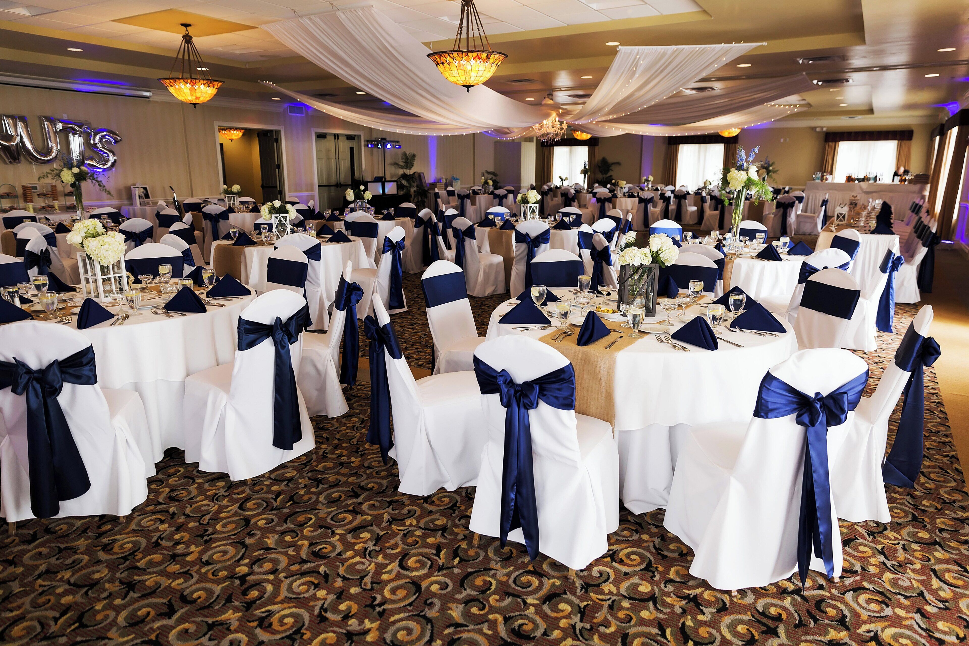 A banquet hall with round tables, white tablecloths, and navy blue sashes on chairs.