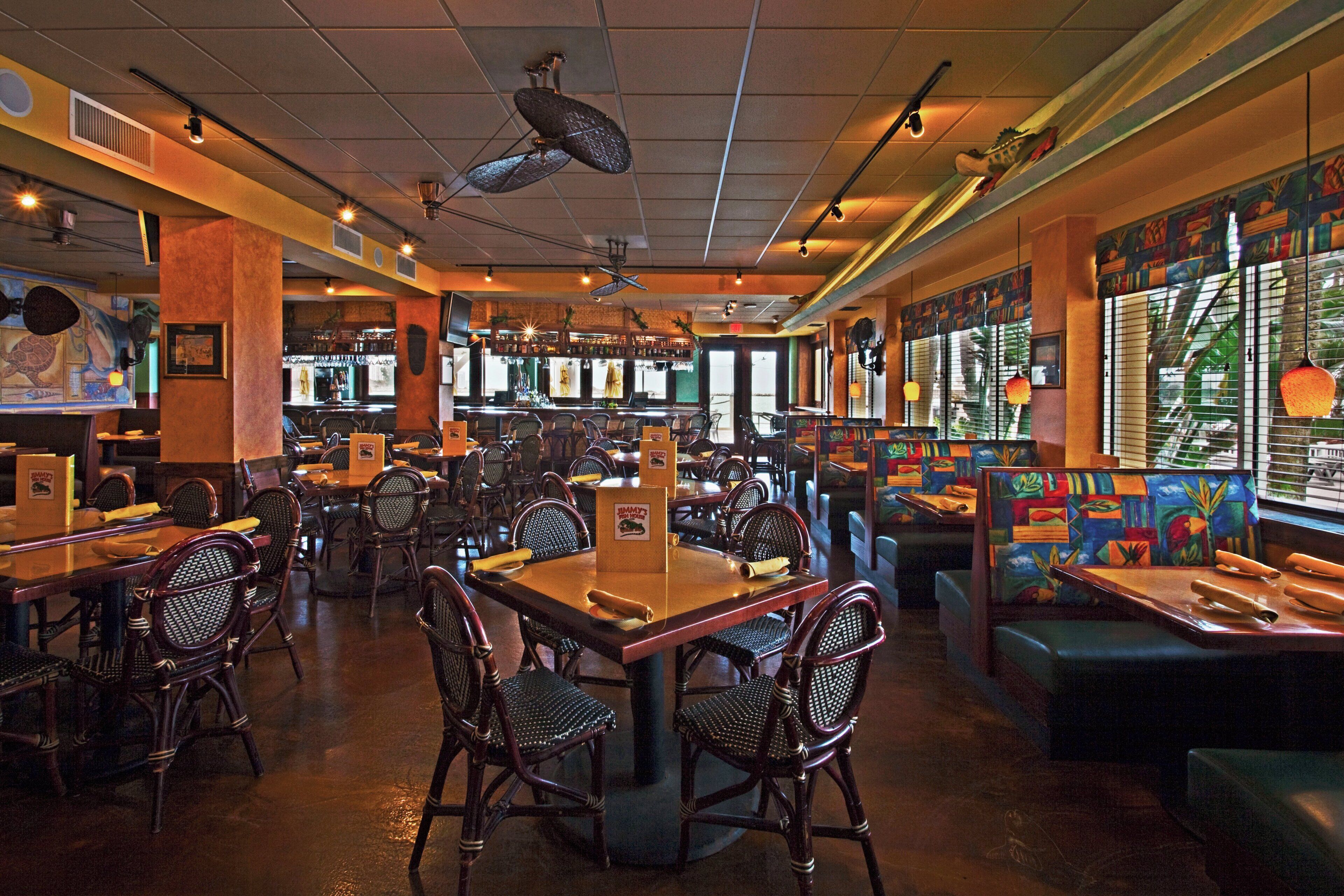 A restaurant interior with multiple dining tables and chairs, a bar area, and a mural on the wall.