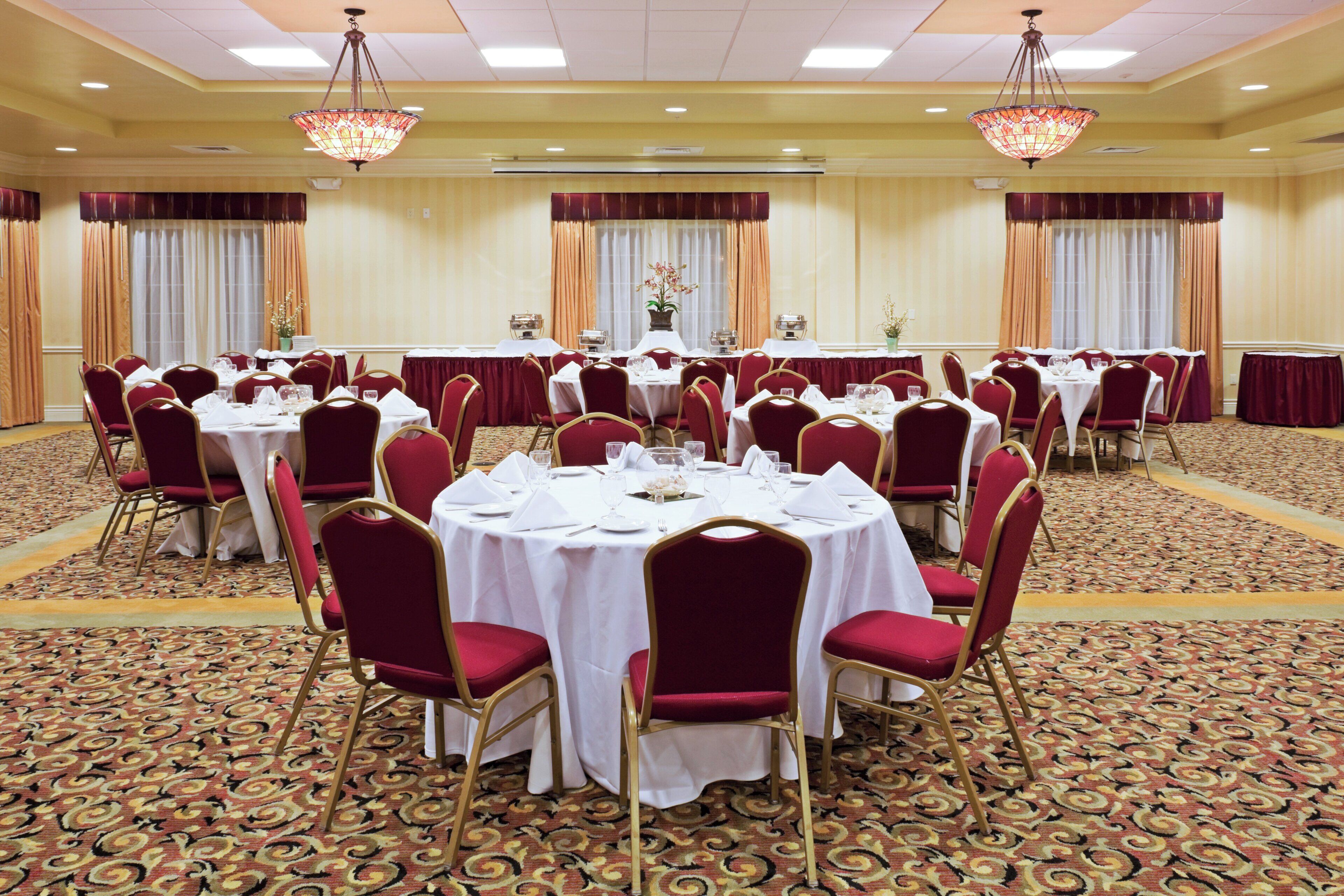 A banquet hall with round tables, red chairs, and chandeliers.