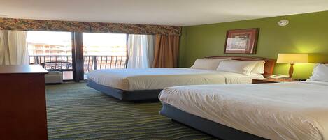 A hotel room with two beds, a desk, a chair, a lamp, and a view of the outside.