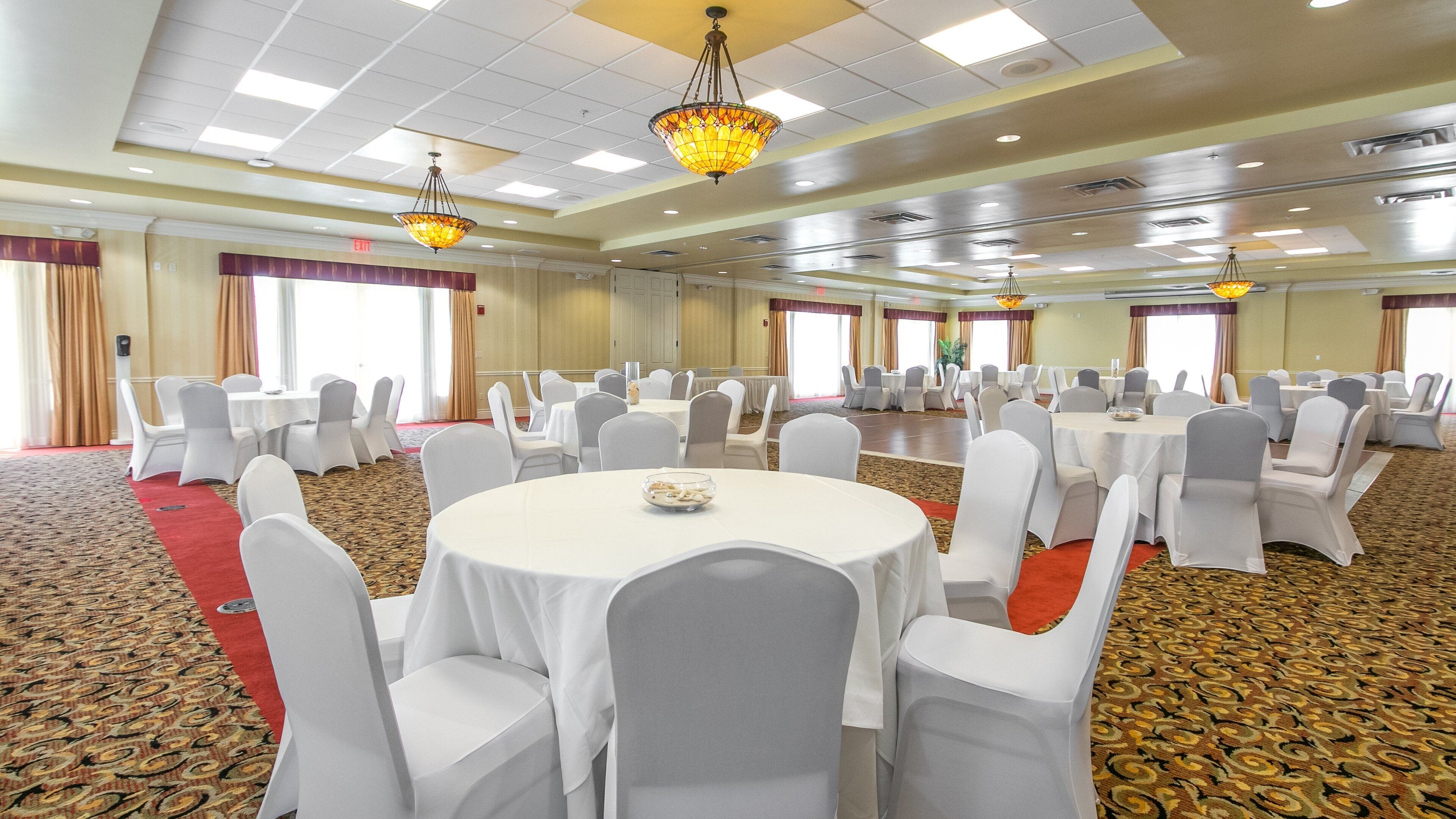 A conference room with round tables, white chairs, and chandeliers.