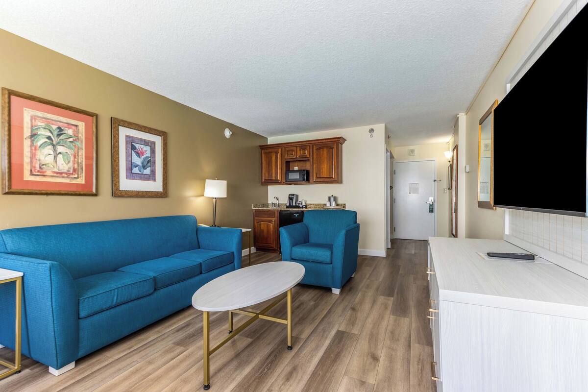 Ein Wohnzimmer mit einem blauen Sofa, einem kleinen Tisch und einer Küchenzeile mit Holzschränken und einer Mikrowelle.