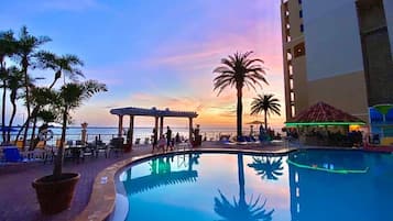 A pool area with a sunset view, palm trees, and a building with balconies.