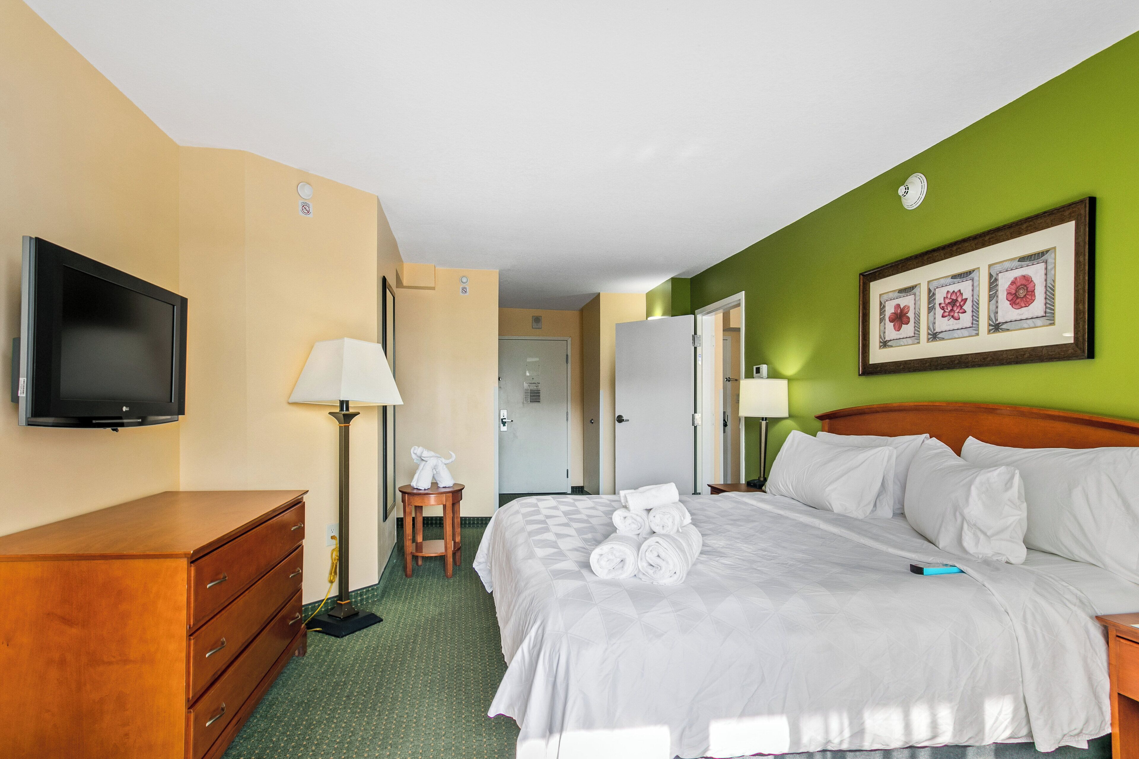 Ein Hotelzimmer mit Bett, Fernseher, Kommode, Lampe und einem gerahmten Bild an der Wand.