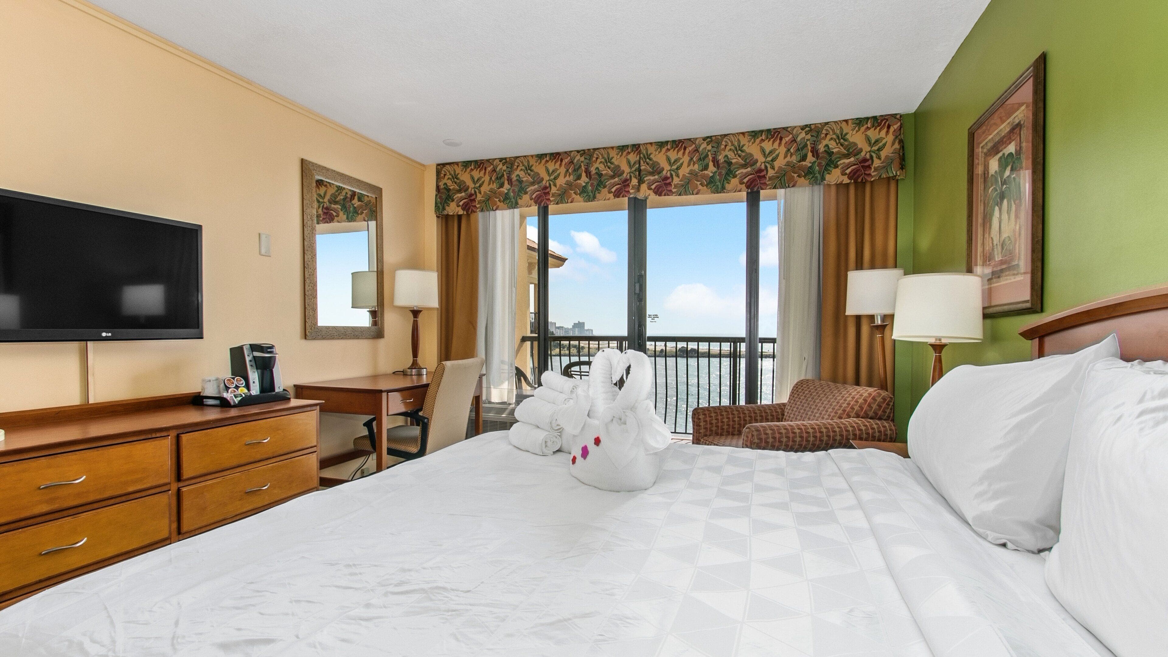 Habitación de hotel con una cama grande, un escritorio, un televisor y vistas al mar.