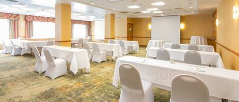 A conference room with multiple tables and chairs, carpeted floor, and a projector screen.