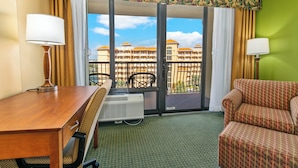 Quarto de hotel com uma secretária de madeira, uma cadeira, um sofá, uma janela com vista para um edifício e uma parede verde.