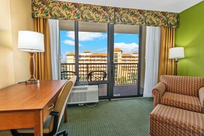 Ein Hotelzimmer mit einem Holzbüro, einem Sessel, einer Couch, einem Fenster mit Blick auf ein Gebäude und einer grünen Wand.