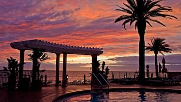 Relax by the pool with a clear ocean view, surrounded by palm trees and a shaded pergola.