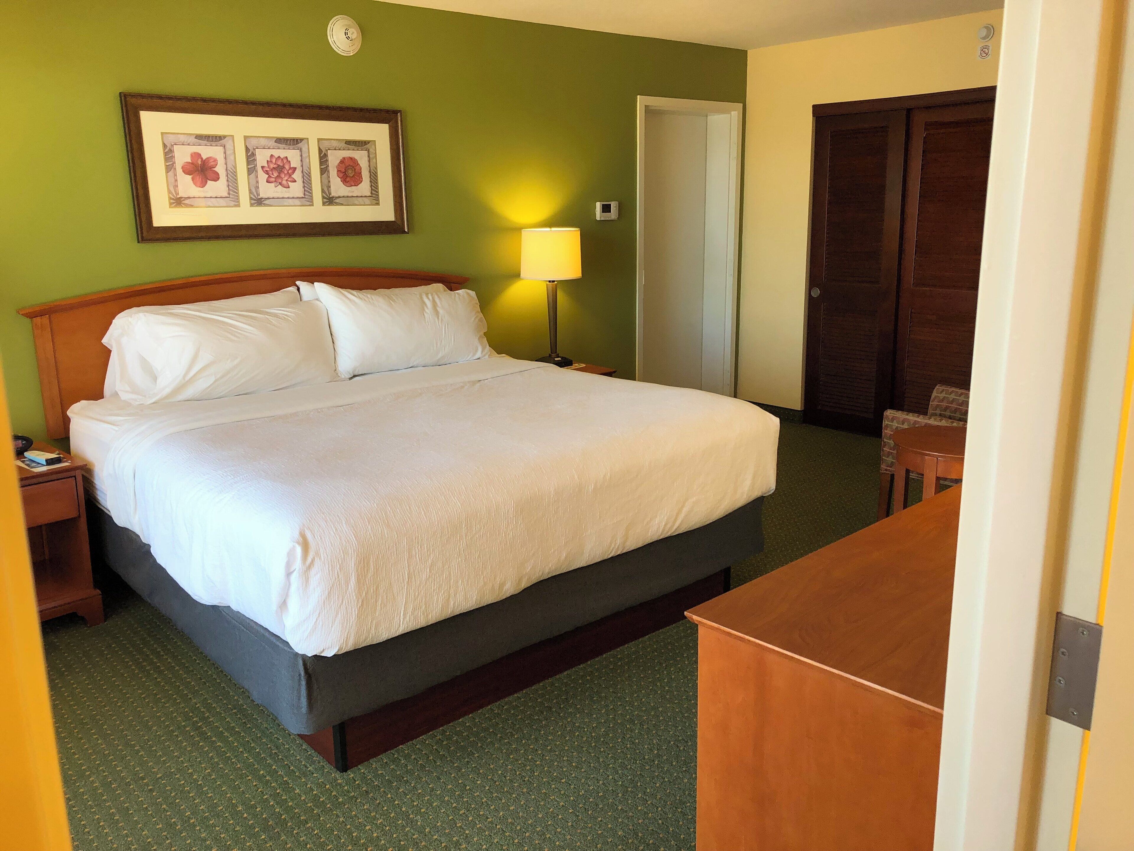 A hotel room with a bed, a nightstand, a lamp, a desk, and a wardrobe.