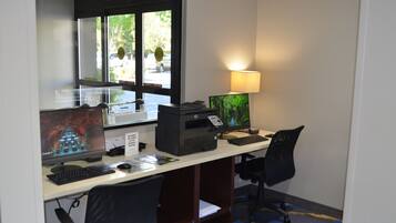 Una oficina de hotel con una computadora de escritorio, una impresora y una lámpara.