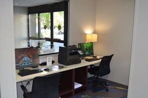 Una oficina de hotel con una computadora de escritorio, una impresora y una lámpara.