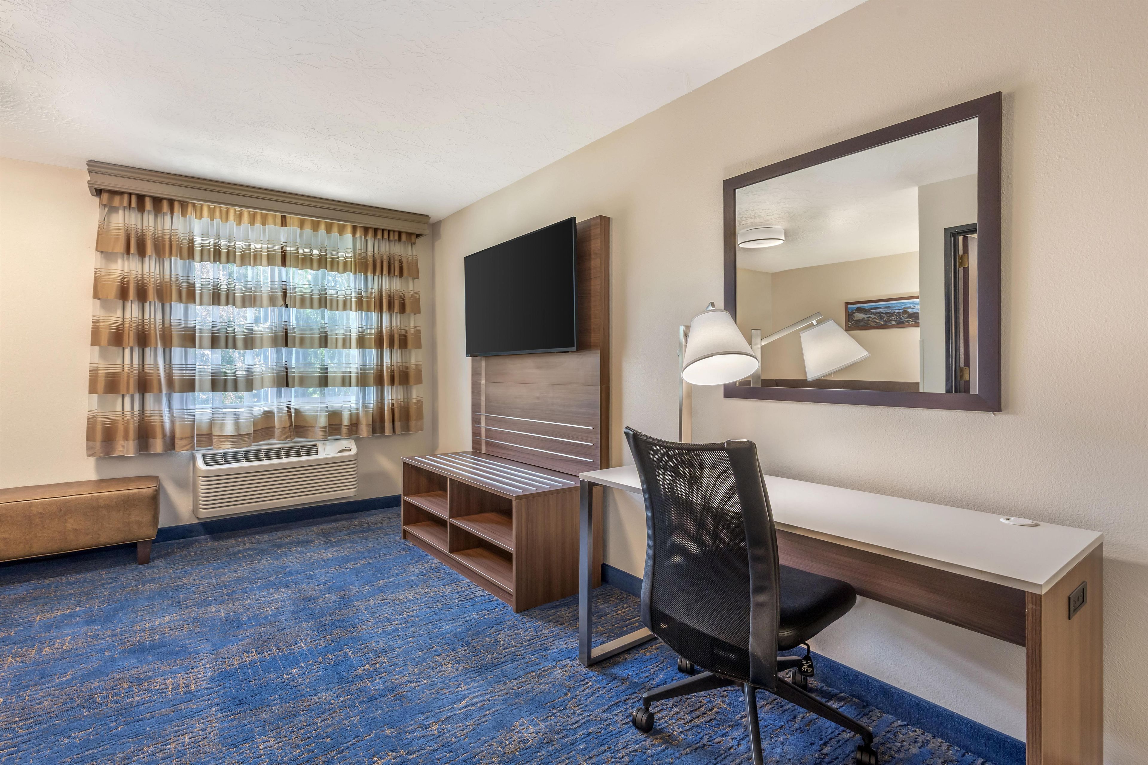 A hotel room with a desk, chair, TV, and a large mirror.