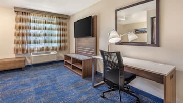A hotel room with a desk, chair, TV, and a large mirror.