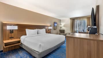 A hotel room with a bed, bedside tables, a desk, a chair, a television, and a painting on the wall.