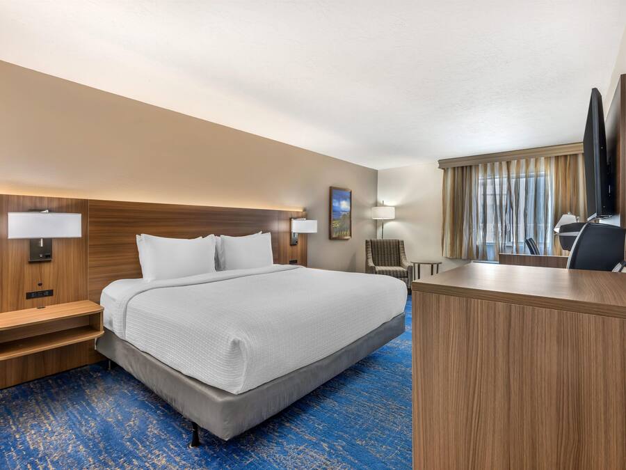 A hotel room with a bed, bedside tables, a desk, a chair, a television, and a painting on the wall.