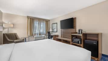 Habitación de hotel con una cama grande, un escritorio, una silla, un televisor, un microondas y un refrigerador.