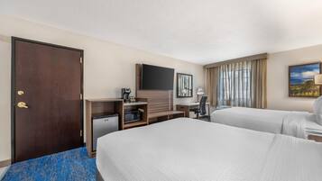 A hotel room with two beds, a desk, a television, and a window with curtains.